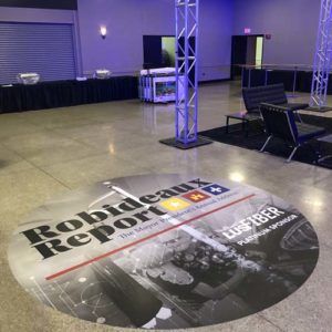 Custom-designed floor graphic by Pixus Digital Printing featuring the 'Robideaux Report' promotional design in an event space with chairs and lighting structures.